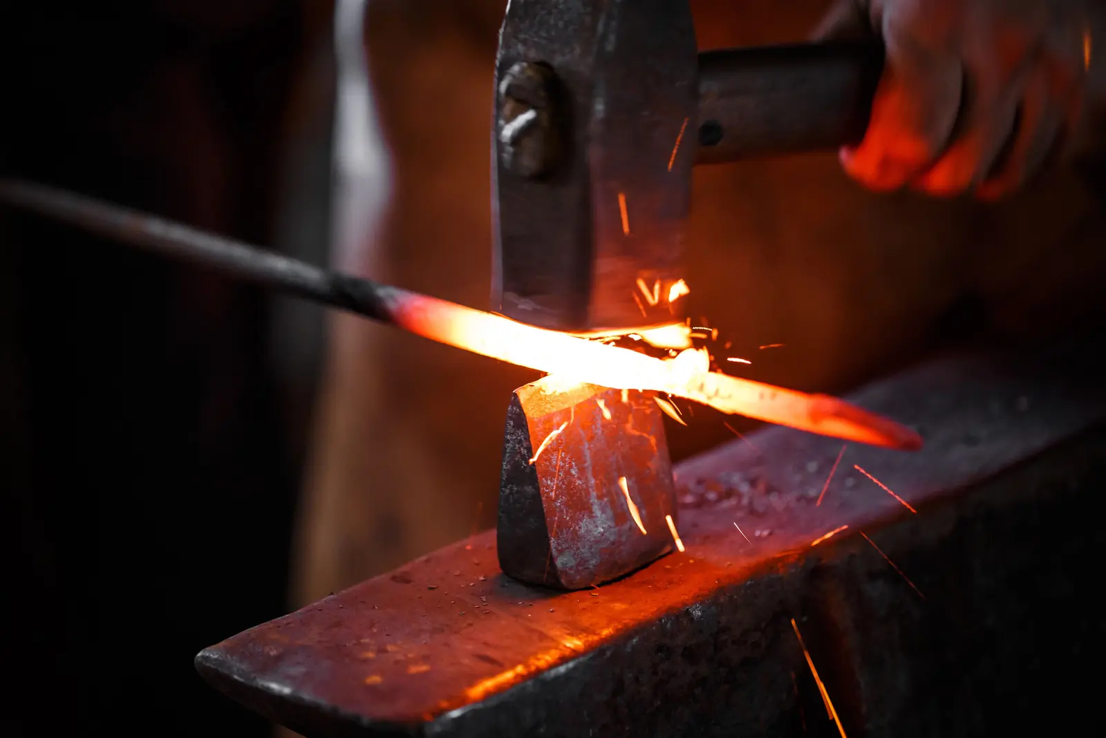 A hammer striking a glowing steel bar on the anvil, sparks flying